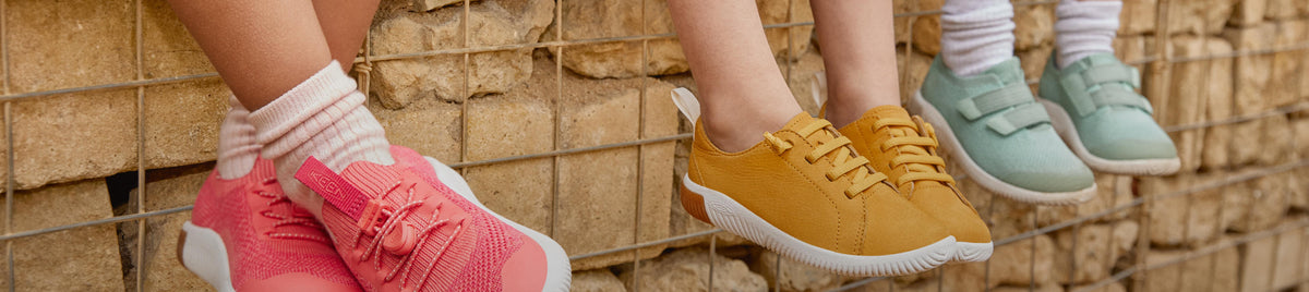Kniehohes Bild von drei Kindern, die auf einer Mauer sitzen und bunte KEEN KNX-Schuhe tragen
