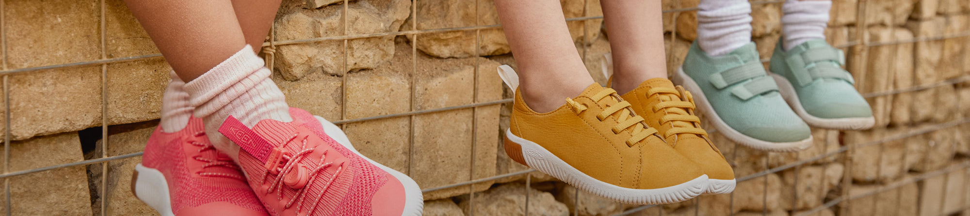 Kniehohes Bild von drei Kindern, die auf einer Mauer sitzen und bunte KEEN KNX-Schuhe tragen