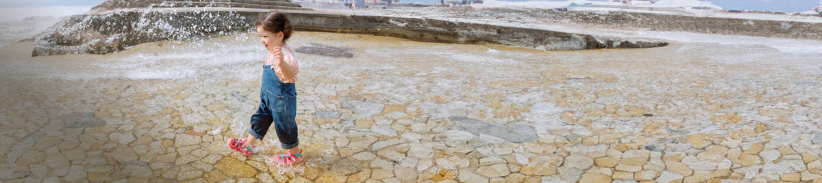 Kleinkind spritzt Wasser auf Sandsteinplatten in KEEN-Wassersandalen.
