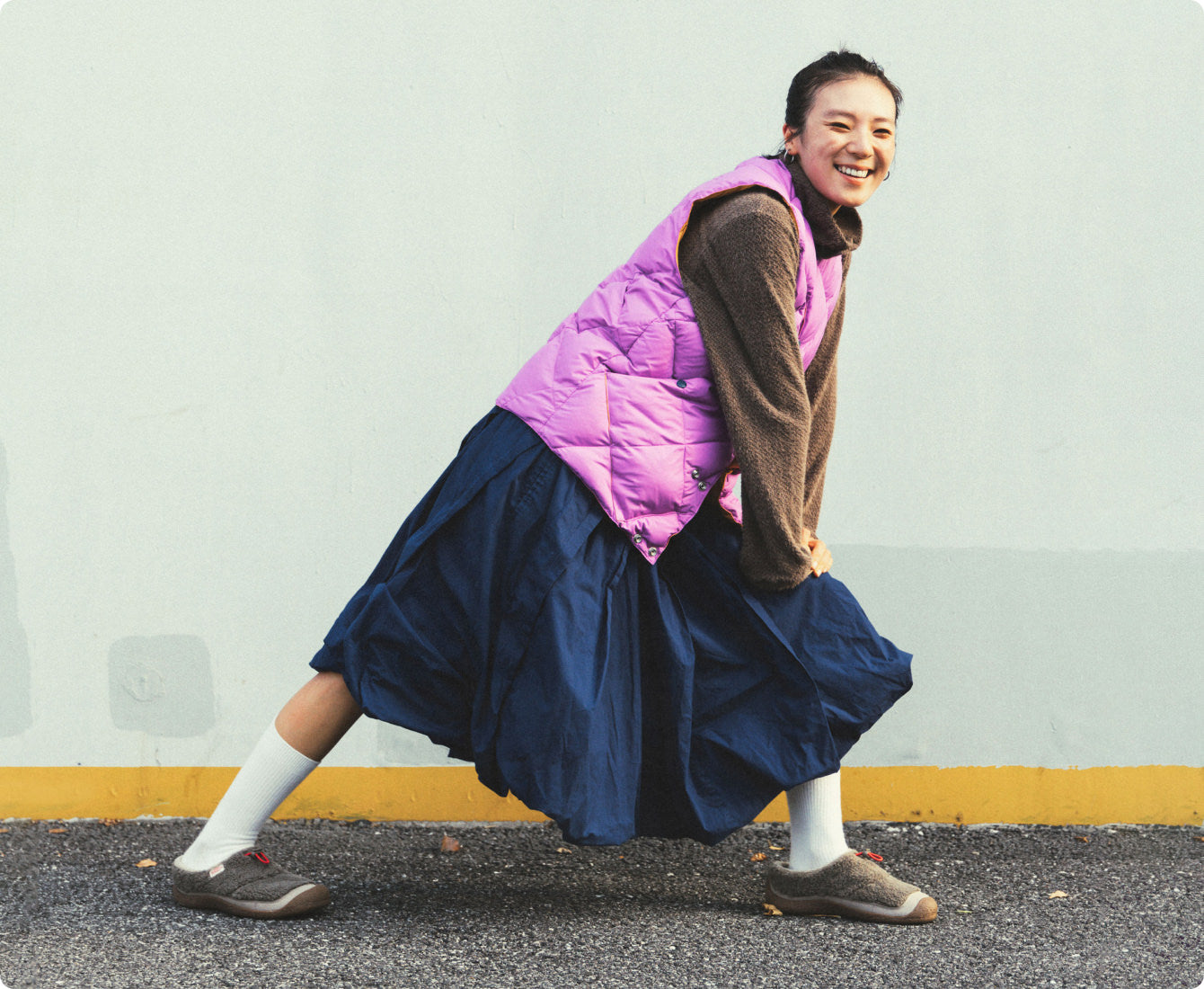 Frau in pinker Weste und weitem Rock lacht und trägt gemütliche KEEN Howser Slipper.
