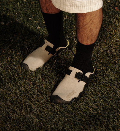 Beige Slip-ons mit schwarzen Riemen  von KEEN x Metalwood auf Gras 