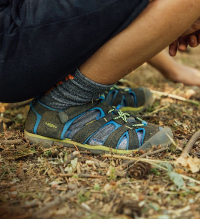 Graue und blaue KEEN Kids-Sandale beim Spielen im Wald.