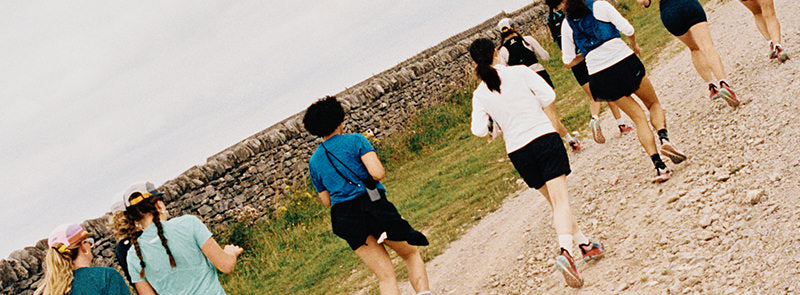 Gruppe von Läuferinnen joggt auf Kiesweg entlang einer Steinmauer und trägt leichte KEEN Trail- und Run-Schuhe.