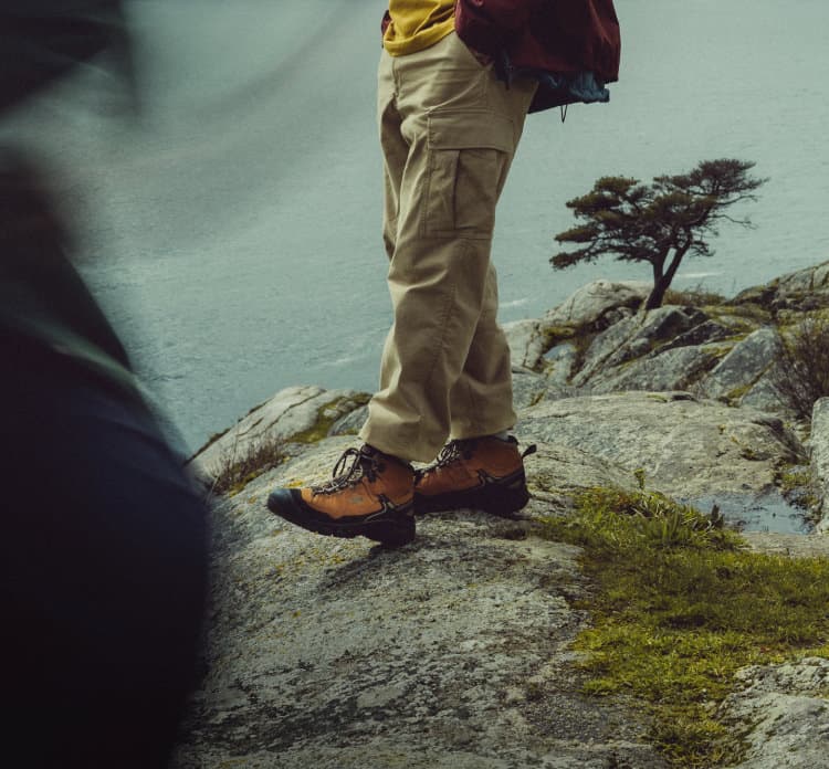 Wanderer in KEEN Trekkingschuhen auf Felsklippe mit Blick aufs Meer - wasserfeste Hiking-Boots für Küstenwanderungen