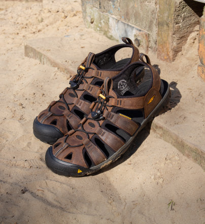 Ein Paar braune Clearwater-Sandalen aus Leder im Sand.