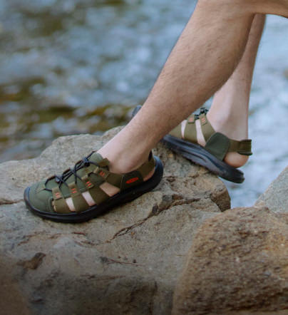 Mann kniet auf einem Felsen und trägt grüne Seanik Sandalen