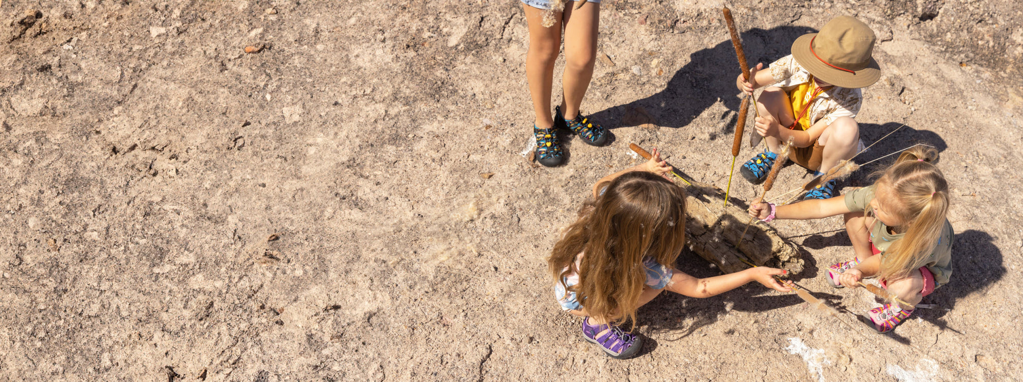 Kinder spielen mit Holz im Sand und tragen Newport- und Seacamp-Sandalen