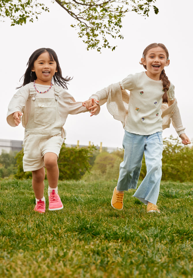 Kinder tragen KNX-Schuhe, halten sich an den Händen und rennen in der Natur.