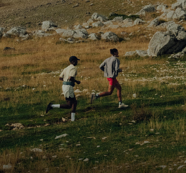 Zwei Trailrunner laufen über eine steinige Wiesenlandschaft im Gebirge, Fokus auf Bewegung, Tempo und Outdoor-Running.