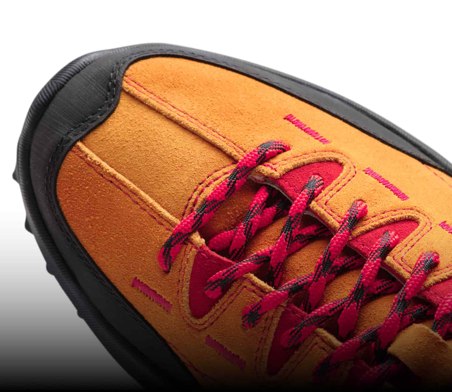 Schwarze Schuhspitze eines orangen Veloursledersneaker mit roten-schwarzen Schnürsenkeln und roten Details. 