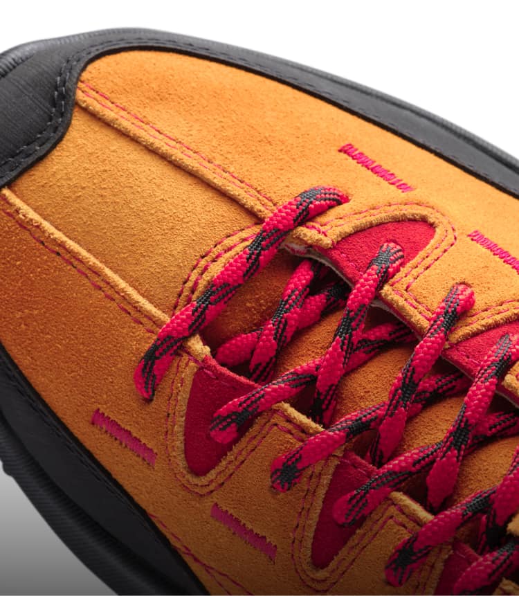 Schwarze Schuhspitze eines orangen Veloursledersneaker mit roten-schwarzen Schnürsenkeln und roten Details. 
