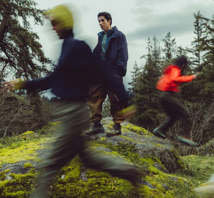 Person in Outdoor-Kleidung und KEEN Wanderschuhen auf grünen Steinen im Wald mit dynamischen Effekten
